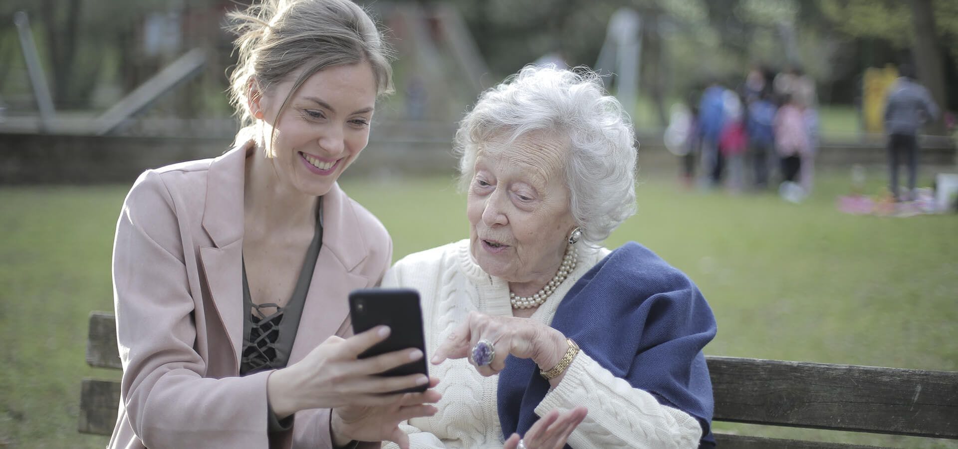 Chica enseñando a persona mayor como funciona un móvil en un parque